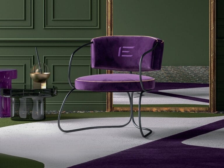 A modern purple velvet chair with black metal legs sits on a geometric-patterned rug in a green room with decorative wall molding and a glass side table.
