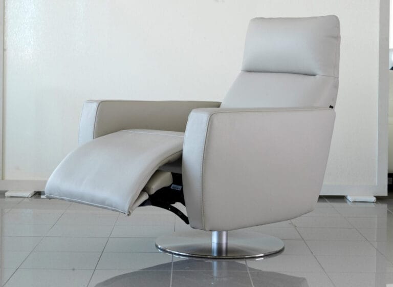 A modern light gray reclining chair with a metal swivel base is positioned on a tiled floor against a plain background.