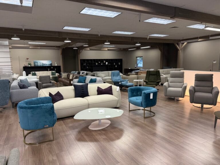 A modern furniture showroom with various sofas, armchairs, and tables arranged on a wooden floor under bright ceiling lights.