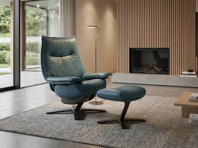 A modern living room features a blue leather lounge chair with matching ottoman on a gray rug, near a floor lamp, fireplace, and wood-paneled wall.
