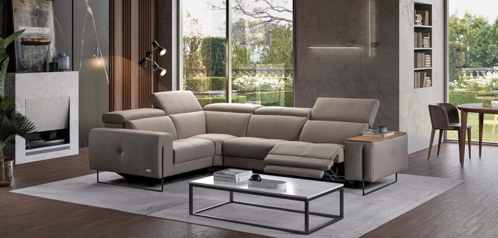 Modern living room with a beige sectional sofa featuring a recliner, a marble coffee table, and large windows overlooking a garden.