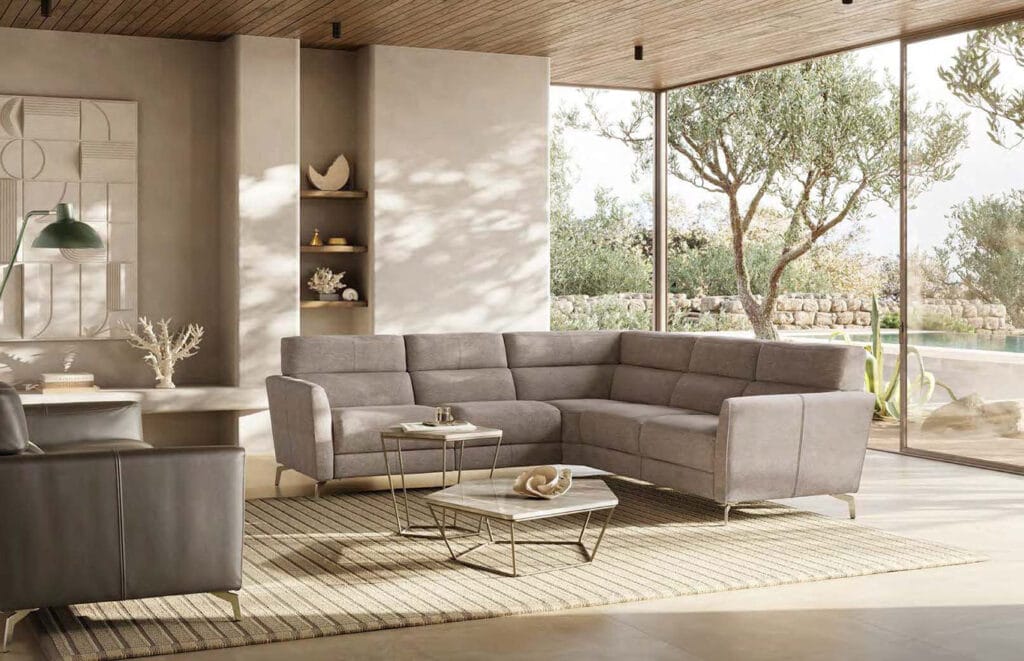 Modern living room with a grey sectional sofa, minimalist decor, large windows, and a view of a garden and pool outside.